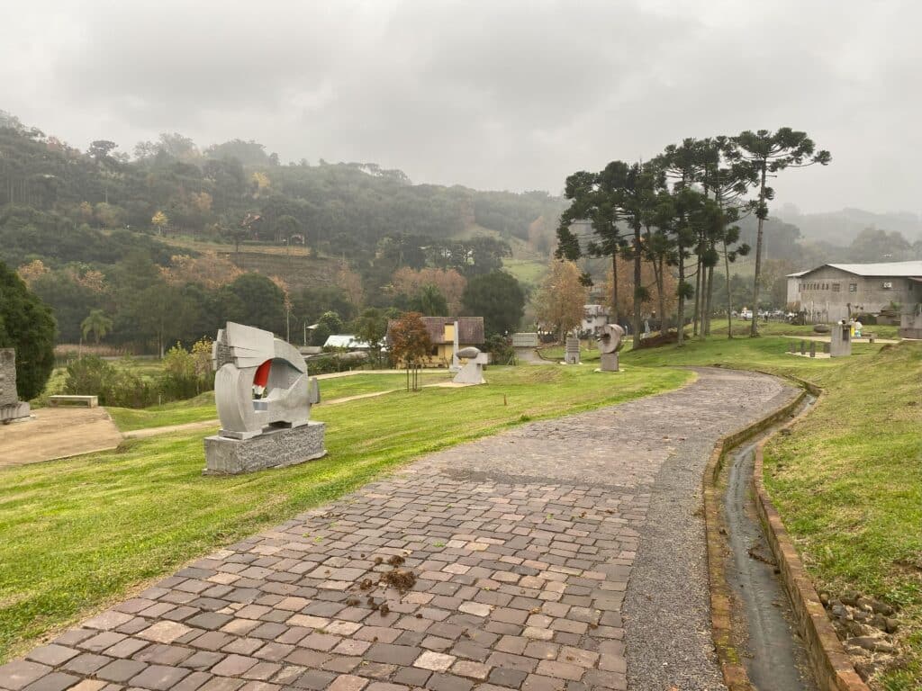 Caminhos entre o gramado, onde se vê esculturas espalhadas por diversos pontos, para serem apreciadas no Parque das Esculturas, em dia chuvoso