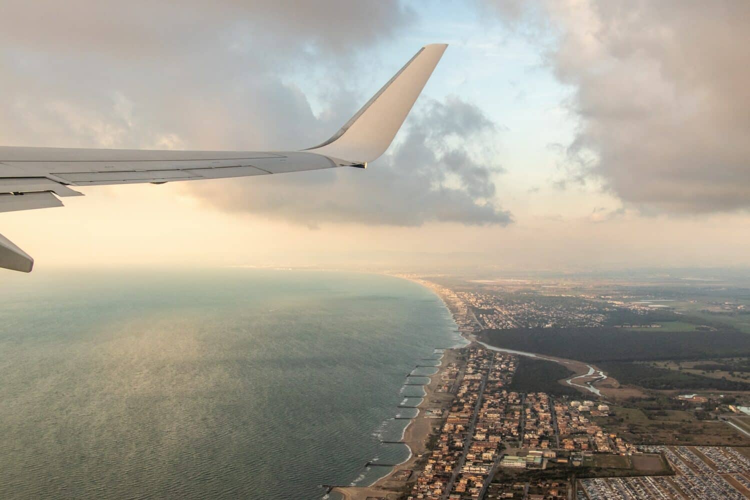 vista da asa de avião passando por cima do Fiumicino, uma cidadezinha à beira-mar, para ilustrar o post de aluguel de carros no Aeroporto de Roma