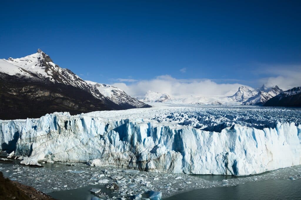 Imagem da Geleira Perito Moreno. O lago na frente, atrás a geleira e ao redor as montanhas.