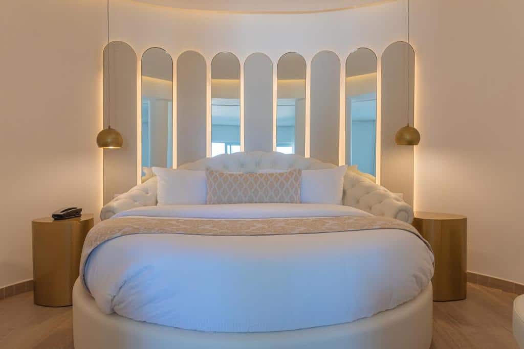 Cama redonda na suíte de lua de mel do Grand Bavaro Princess, uma das escolhas de onde ficar em Punta Cana. Um ornamento de espelhos está na parede atrás da cama, e mesinhas de cabeceira estão dos dois lados.