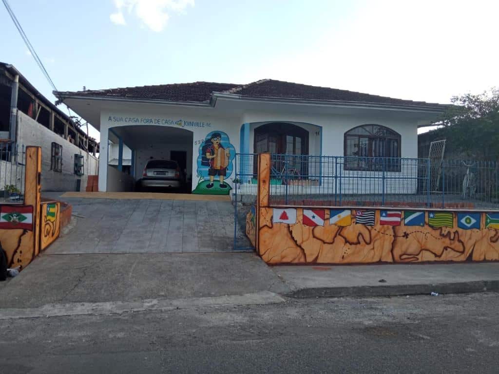 fachada do Hostel e Pousada Boa Vista mostrando o muro pintado com bandeiras de diferentes países, além da rampa de entrada para carros.