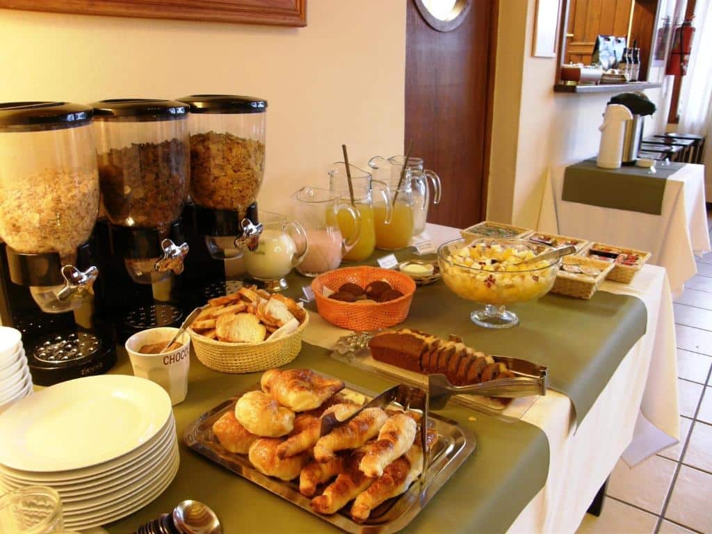 Mesa do café da manhã com pães, cereais, sucos, bolo, frutas e pratos do Hotel Austral Ushuaia.