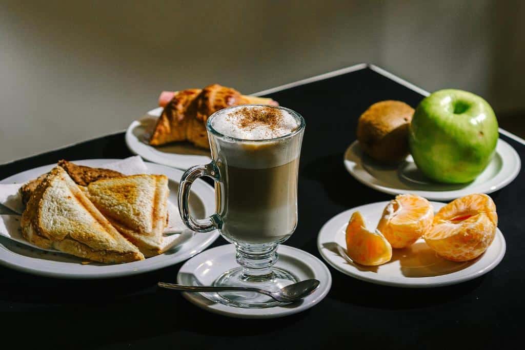Café da manhã do Hotel Tierra del Fuego. Uma mesa preta com pratos com pães, frutas e um capppuccino.
