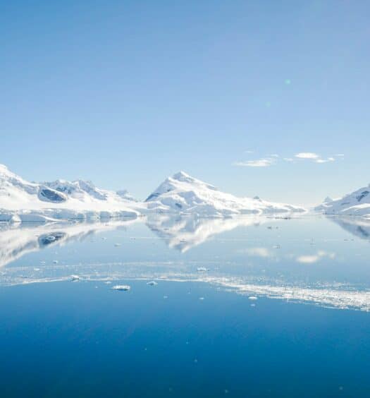 Vista da Ilha Elefante na Antártida durante o dia com lago congelado e ao fundo montanhas cobertas de neve. Representa seguro viagem Antártida.