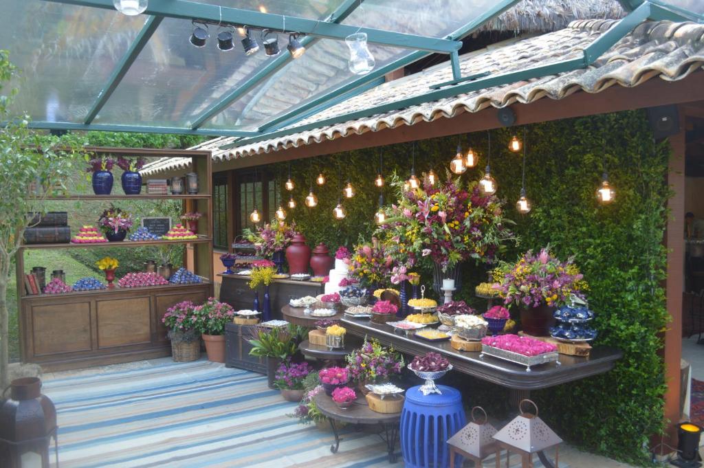 Jardim do Pousada Les Roches com mesinhas enfeitadas com vasos, flores coloridas e docinhos sendo servidos, em uma área coberta e com iluminação indireta