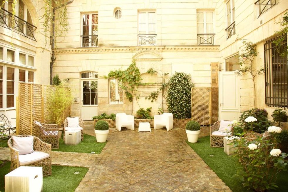 Área comum ao ar livre do L'Hôtel Particulier Bordeaux.  É possível ver várias cadeiras dispostas ao redor do caminho central. Há também algumas plantas decorando o ambiente.
