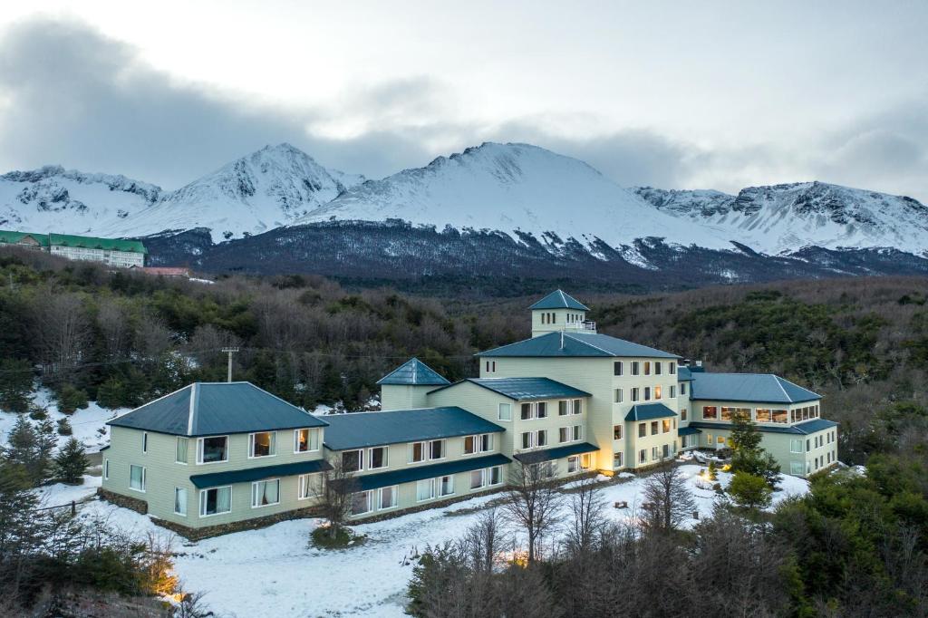 Los Acebos Ushuaia Hotel de fora. O hotel no meio, ao redor área verde e no fundo, as montanhas com neve.