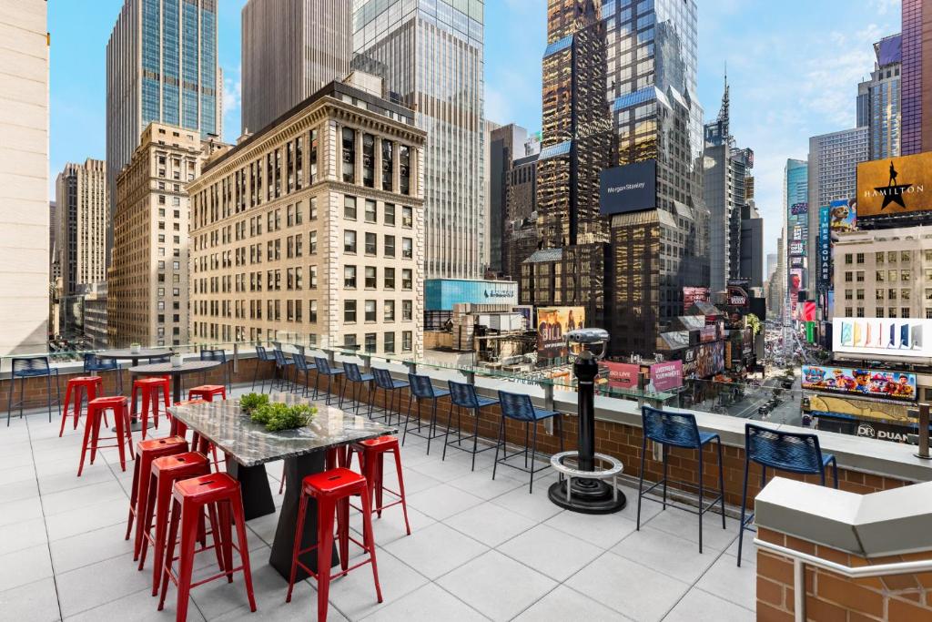 Terraço na cobertura do M Social Hotel Times Square New York com vista direta para a Times Square, no terraço há cadeiras, mesas e banquinhos, além de um binóculo de chão