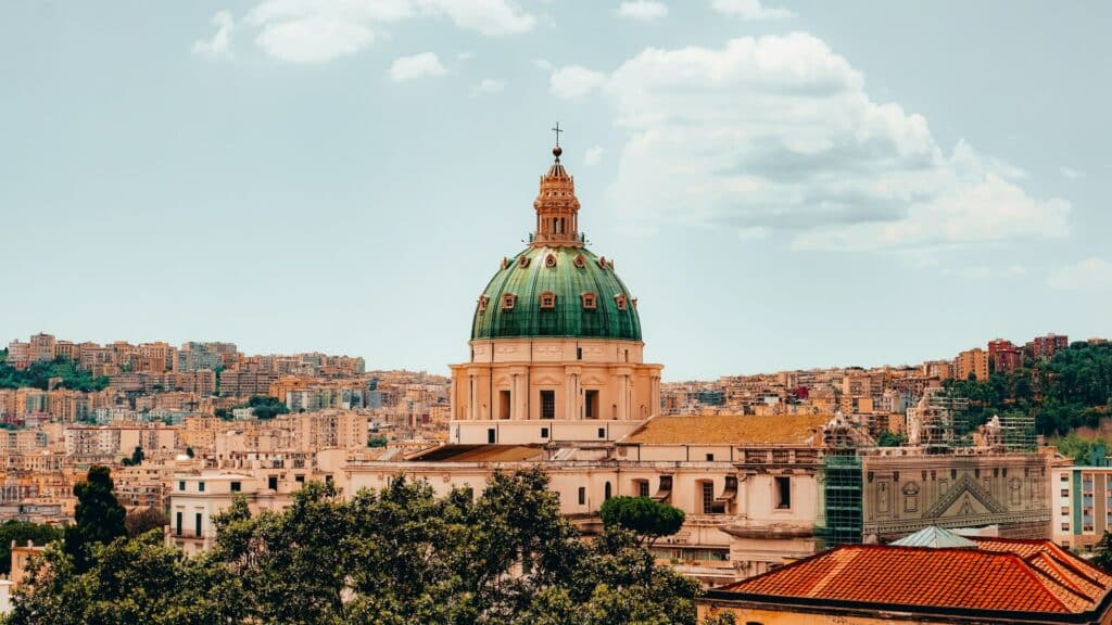 Cúpula da Basilica dell'Incoronata Madre del Buon Consiglio com detalhes verdes e em volta várias construções da cidade de Nápoles durante o dia, imagem ilustrando post Hotéis em Nápoles.
