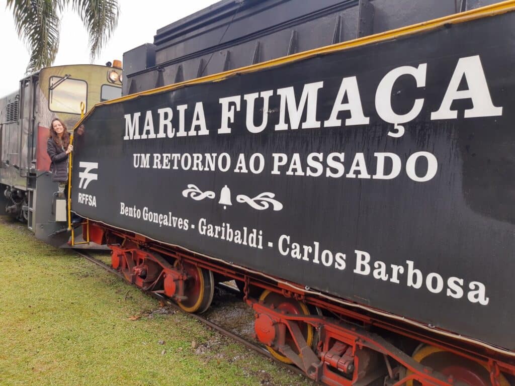 Vagão principal da Maria Fumaça, uma das opções de o que fazer em Bento Gonçalves, vista por fora, com a editora (Nátalie) vista ao fundo, sobre a escadinha de acesso