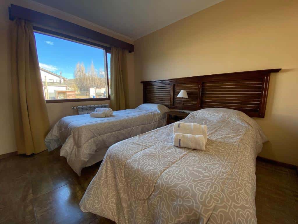 Quarto da Patagonia Austral Suites. Duas camas de solteiro com toalhas em cima, entre elas uma cômoda com abajur. No lado esquerdo, no fundo, uma janela.