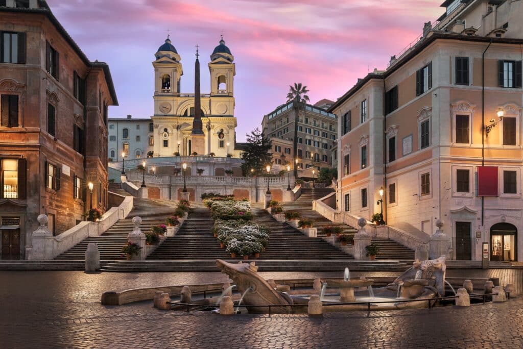 vista à noite do Piazza Spagna, uma das opções do que fazer em Roma, com uma fonte no centro, a Escadaria Espanhola que culmina em uma igreja