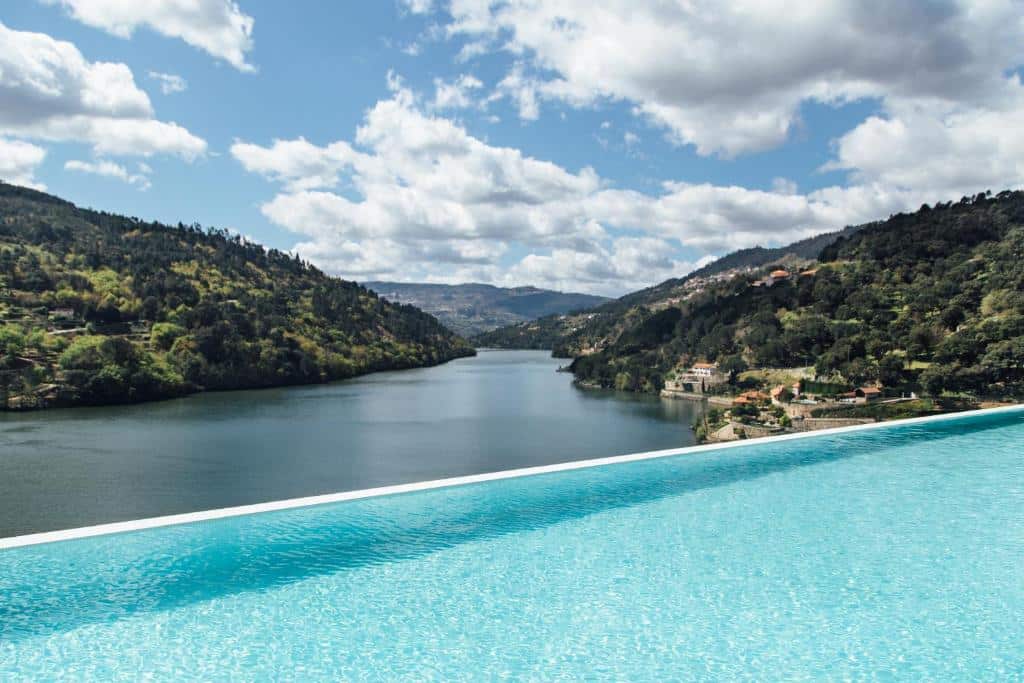 Vista da piscina do Douro Royal Valley Hotel & Spa durante o dia com piscina a frente com vista para o rio Douro e a região.