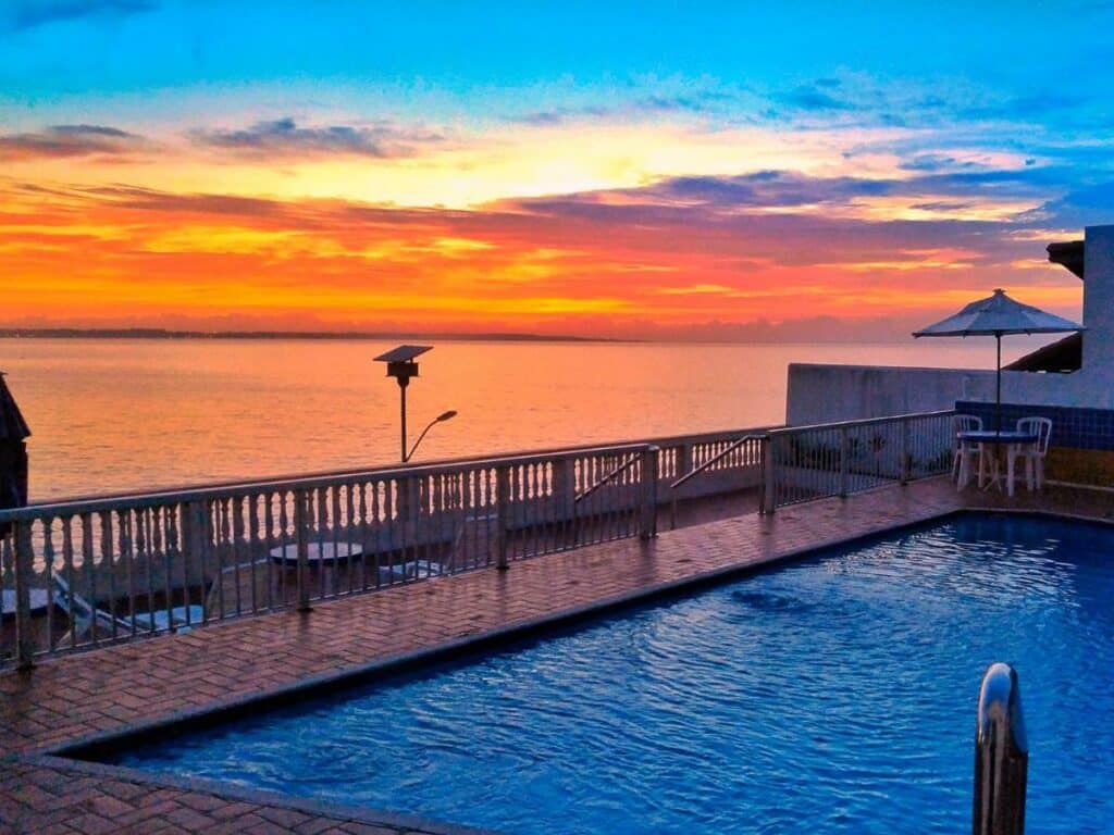 Piscina do Hotel Portal da Lua. Uma piscina ao ar livre na frente, no lado esquerdo uma escada com uma sacada e uma mesinha para apreciar o pôr do sol no mar.