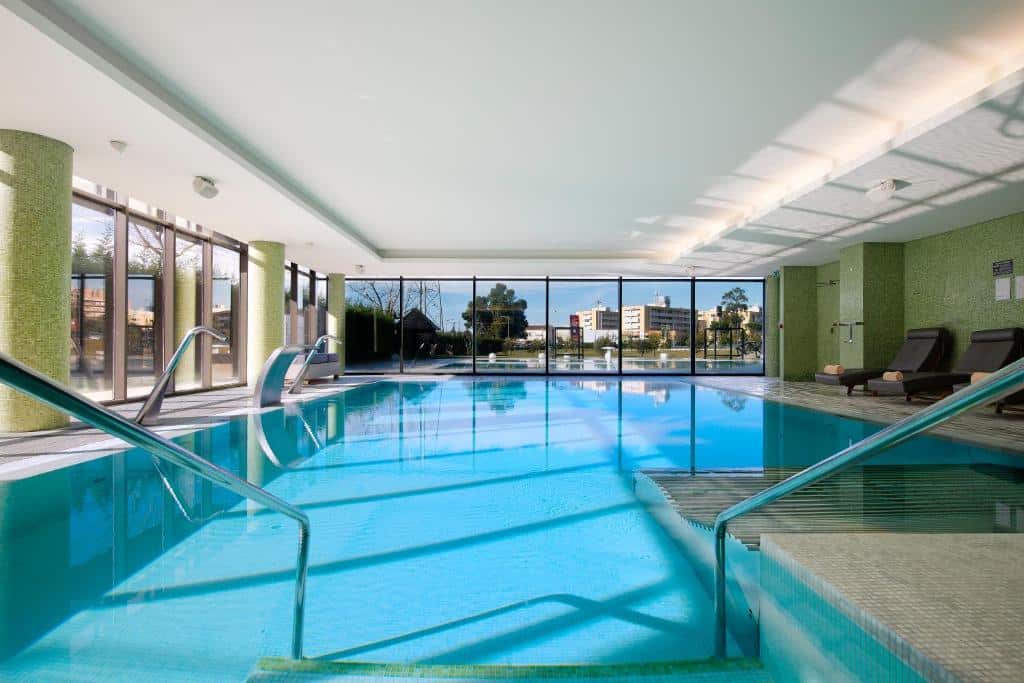Piscina coberta do Melia Braga Hotel & Spa com a piscina no centro do ambiente e do lado direito poltronas.