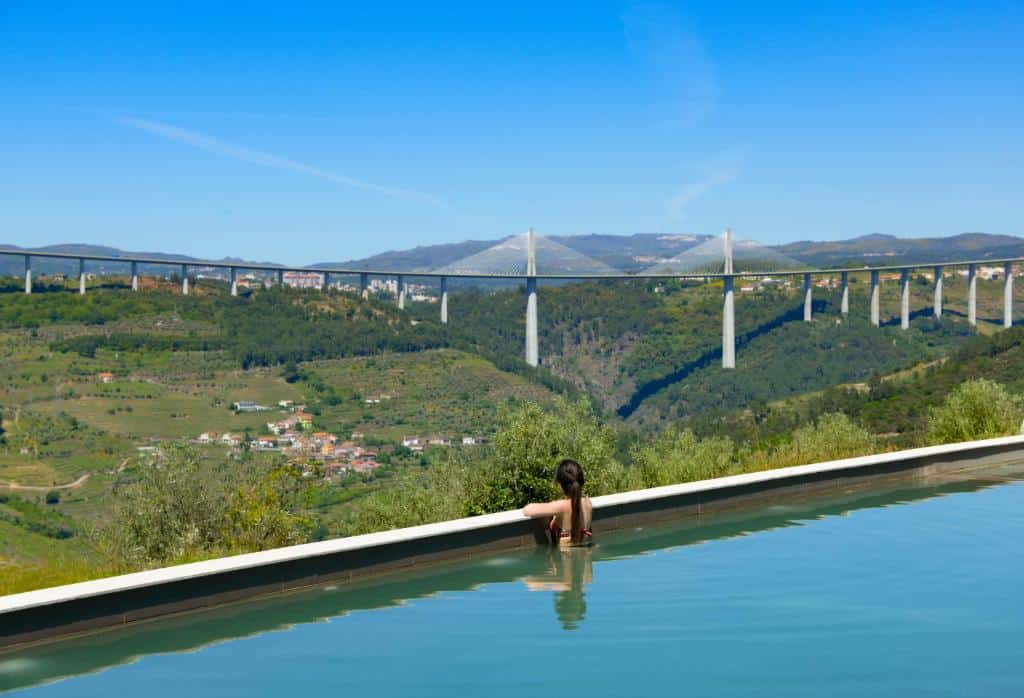 Vista da pisicna do MW Douro Wine & Spa Experience Hotel Collection durante o dia, com piscina a frente com uma mulher dentro da piscina com vista para as montanhas.