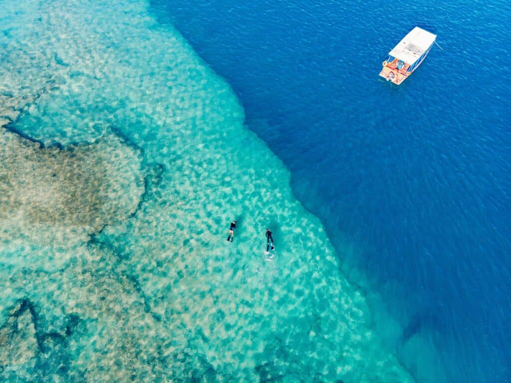 Vista aérea de dois mergulhadores e um barco no mar de águas transparentes, em Marechal Deodoro