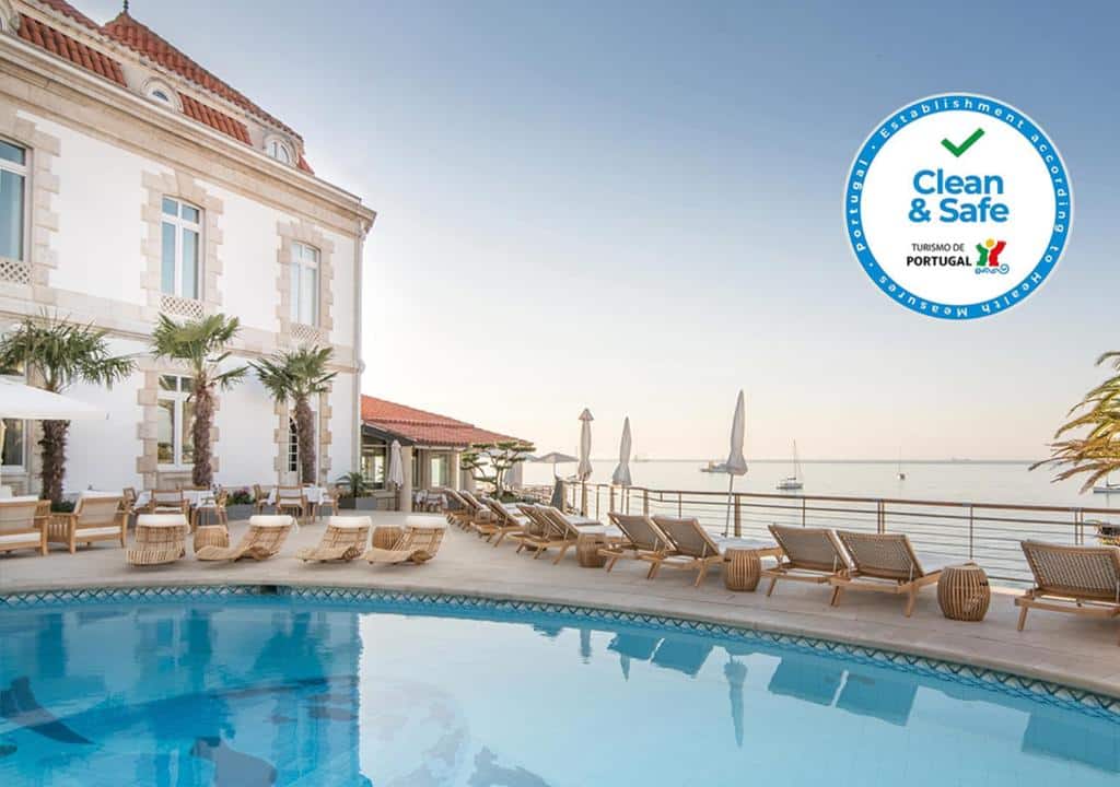 Piscina ao ar livre do The Albatroz Hotel durante o dia com piscina a frente e do outro lado da piscina cadeiras com vista para o mar.