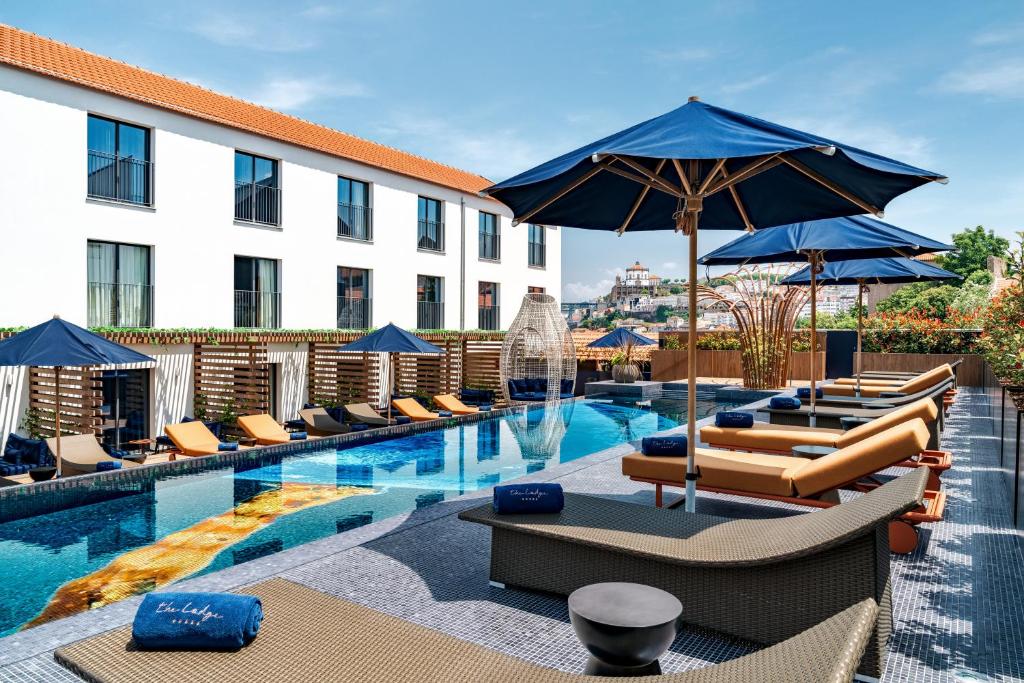 Piscina ao ar livre do The Lodge Porto Hotel com piscina no centro e cadeiras do lado esquerdo e direito da piscina com guarda-sóis.