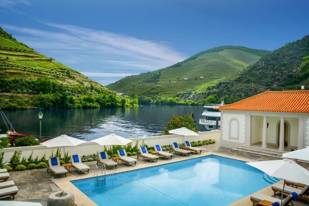 Vista da piscina do The Vintage House – Douro durante o dia com piscina no centro, e em cada lado da piscina cadeiras com guarda-sóis.