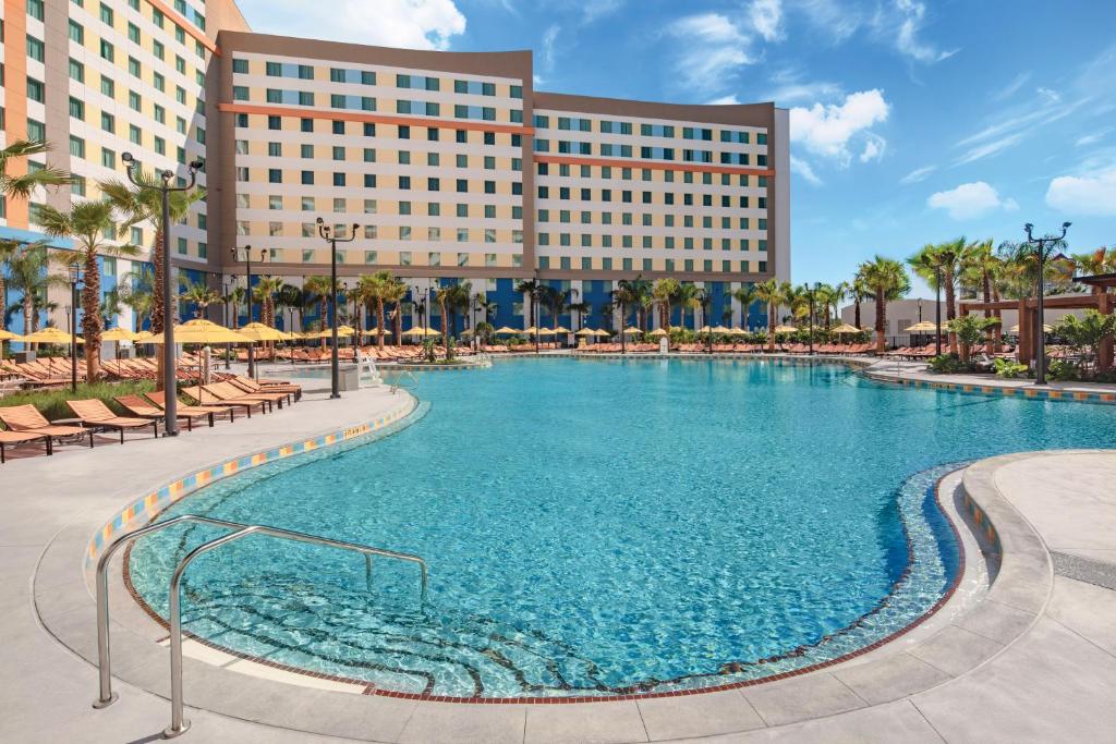 Piscina ampla do Universal’s Endless Summer Resort – Dockside Inn and Suites com um deck cercado por espreguiçadeiras, guarda-sóis e palmeiras