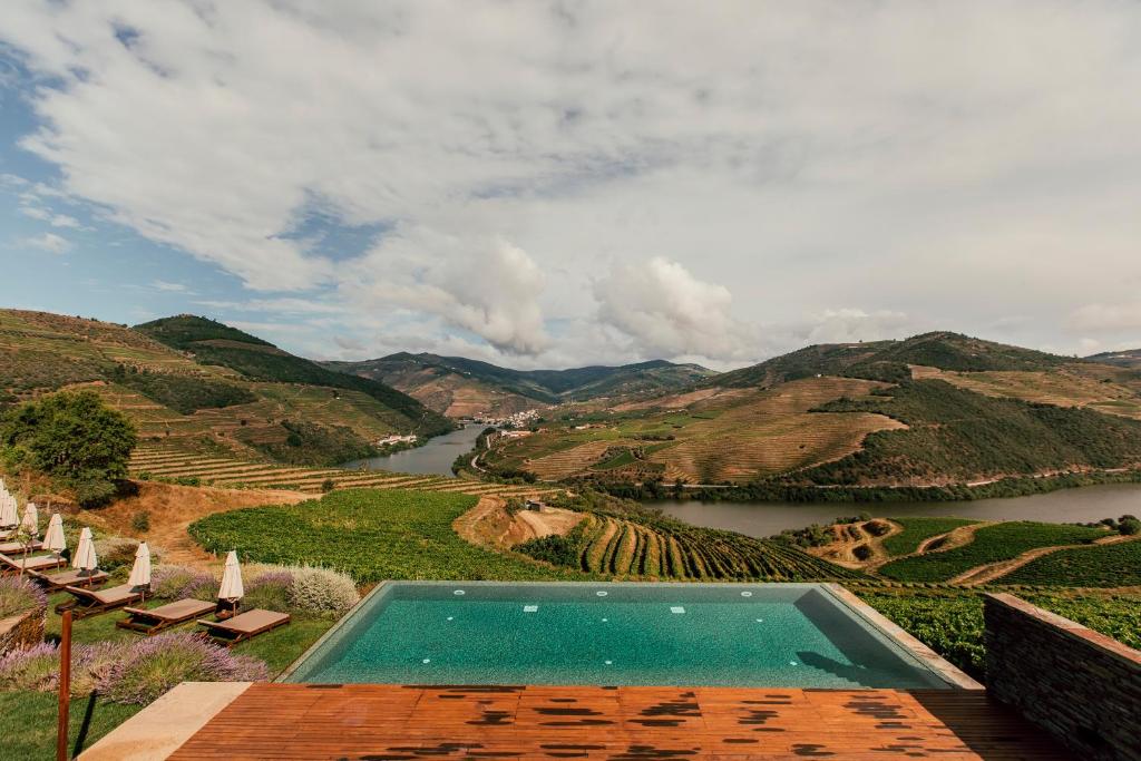 Vista da piscina do Ventozelo Hotel & Quinta durante o dia a frente e ao fundo plantação de vinhas e o rio Douro.