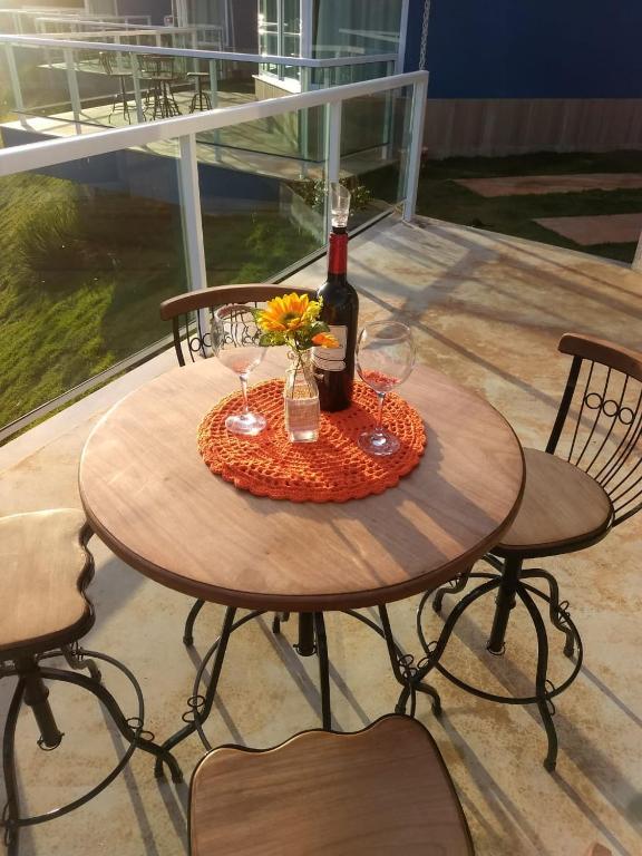 Imagem de uma mesa ao ar livre na Pousada Casa no Sítio. A foto foi tirada de dia, e podemos ver uma mesa com cadeiras em uma varanda na pousada com taças, um vaso com flores e uma garrafa de vinho em cima.