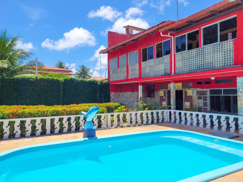 Pousada Villa Coelho. Uma piscina na frente com uma cascata de golfinho. Atrás, do lado esquerdo, um jardim, e do lado direito a pousada.