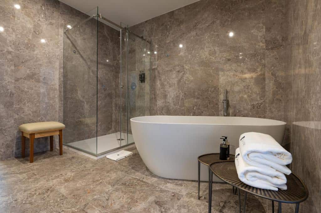 Banheiro com uma banheira oval no Boemio FLH Hotels junto de um box de vidro e um móvel preto com toalhas brancas ao lado da banheira