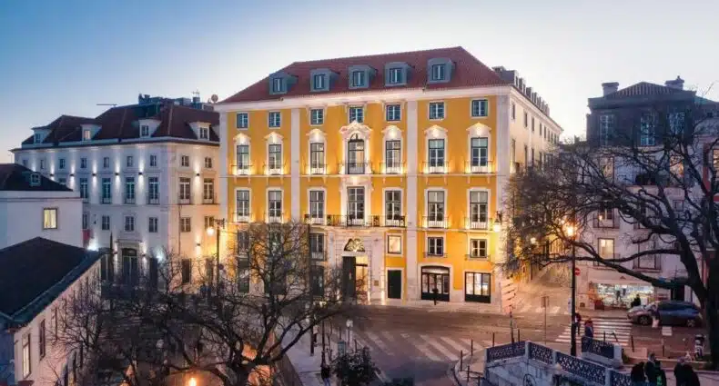 Propriedade do Palácio Ludovice Wine Experience Hotel, uma construção amarela de época com estilo português, com quatro andares, janelas brancas, em uma esquina iluminada, para representar hotéis boutique em Lisboa