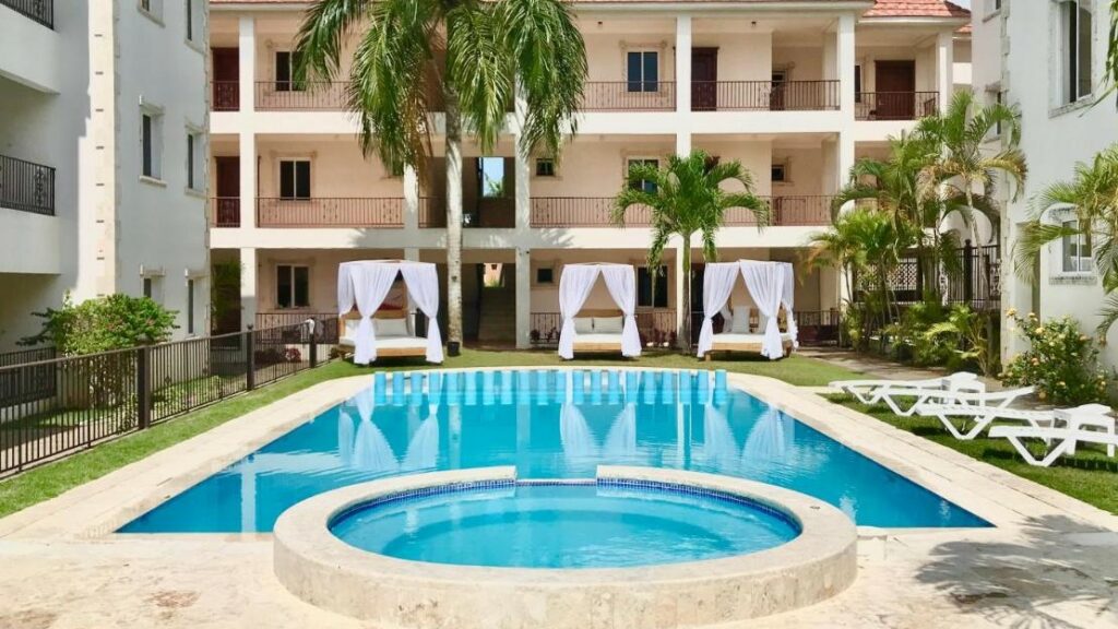 Piscina do Punta Cana Seven Beaches. Espreguiçadeiras e camas balinesas, que são estruturas relaxantes com colchão e cortinas nas laterais, rodeiam a piscina, e os prédios do hotel ficam atrás do local.