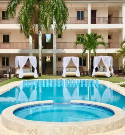 Piscina do Punta Cana Seven Beaches, um dos hotéis baratos em Punta Cana. Espreguiçadeiras e camas balinesas rodeiam a piscina, e os prédios do hotel ficam atrás do local.
