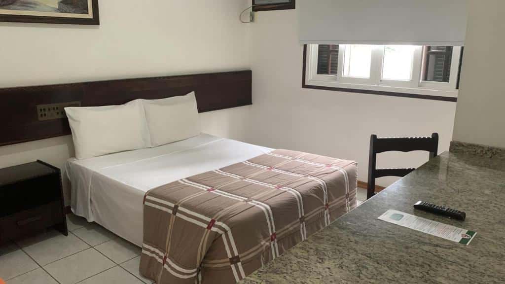 quarto da pousada 7HOLZ em Joinville mostrando uma cama de casal à esquerda e uma mesa de pedra à direita, em frente a cama.