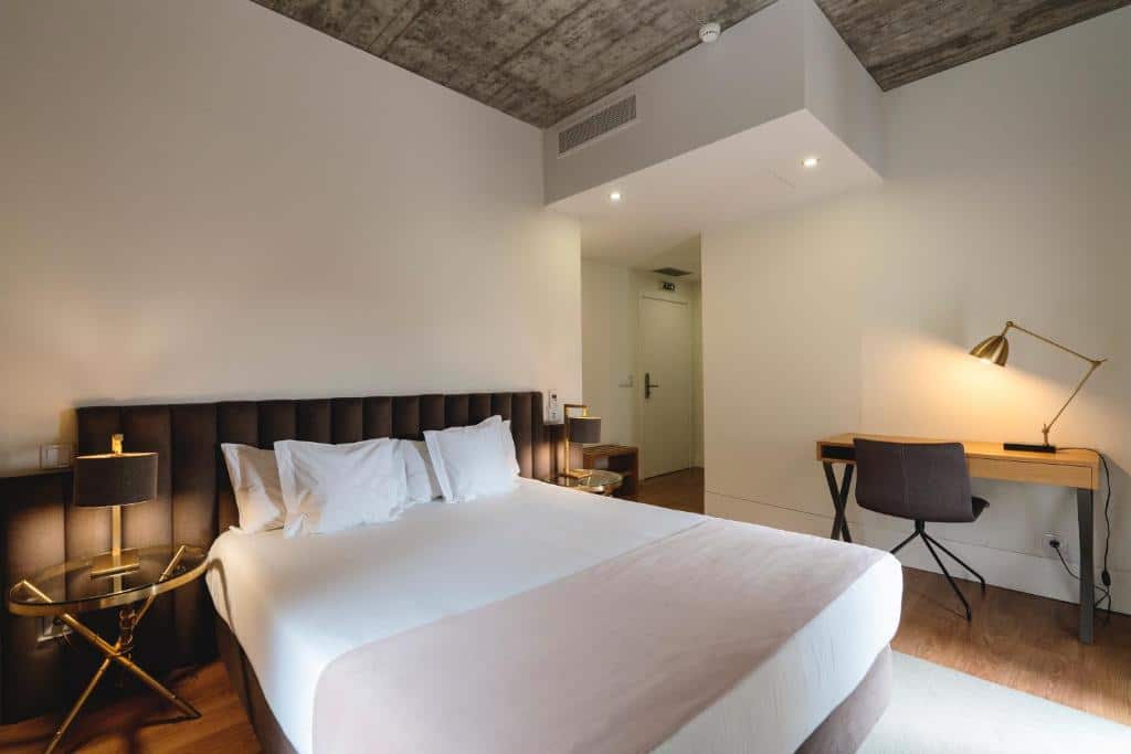 Quarto do Borralha Hotel, Restaurante & Spa com cama de casal do lado esquerdo da imagem com uma cômoda de vidro de cada ado da cama com luminária e do lado direito da cama uma mesa com cadeira.