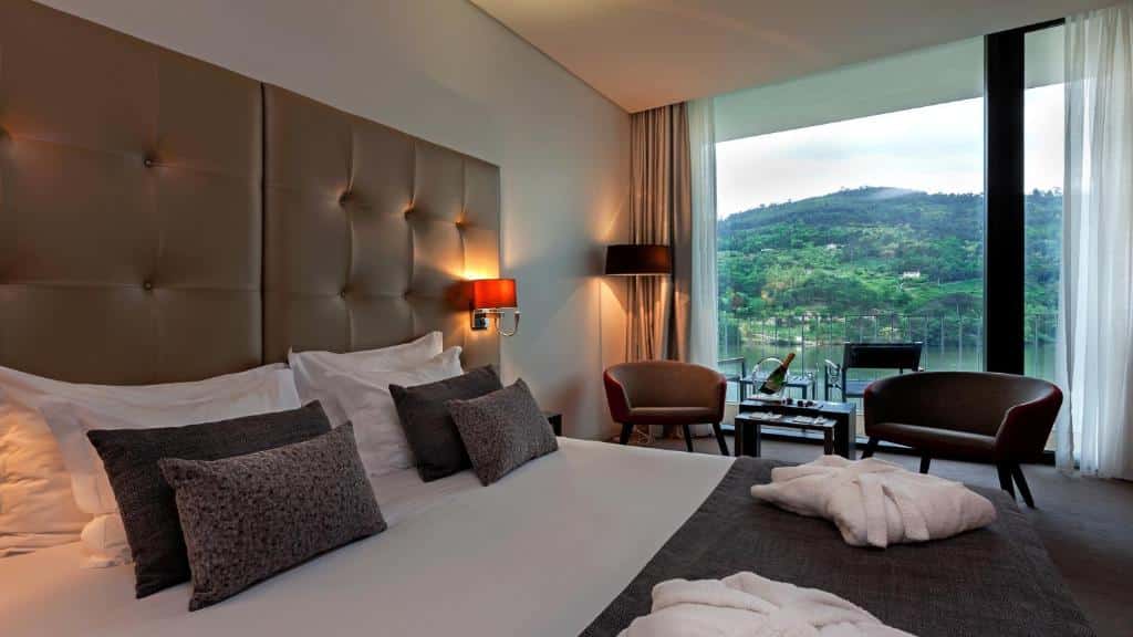 Quarto do Douro Royal Valley Hotel & Spa com cama de casal do lado esquerdo da imagem, do lado direito da cama duas poltronas em cada lado com uma mesa no centro. Representa hotéis para lua de mel em Portugal.