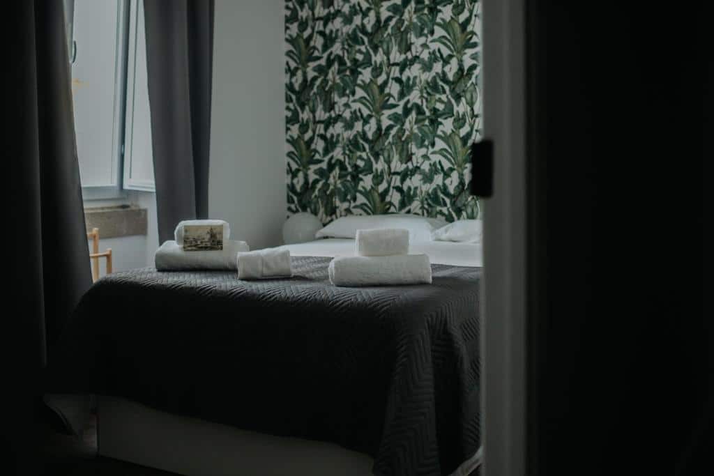 Quarto do hotel Elvas the Queen Residence. O qaurto é pequeno, a cama está centralizada, ao lado esquerdo da cama há um abajur redondo e ainda no lado esquerdo há uma janela com cortinas. Imagem para ilustrar o post hotéis no Alentejo.