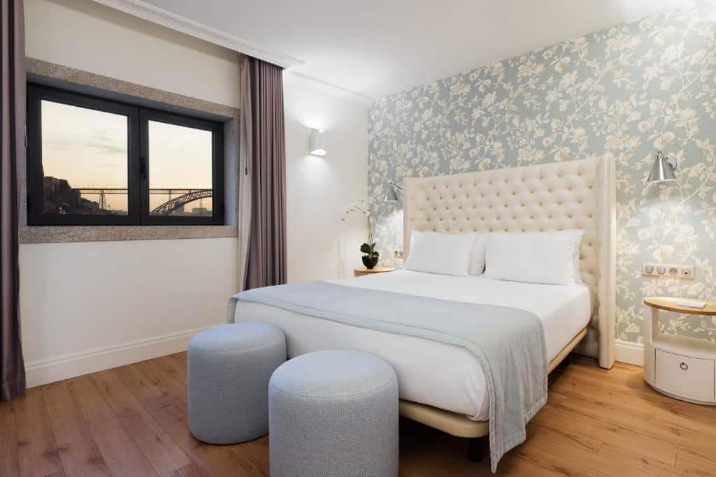 Quarto da Eurostars Porto Douro com cama de casal do lado direito da imagem no centro do quarto com uma cômoda em cada lado da cama, nos pés da cama dois puffs. Representa hotéis com vista do Douro.