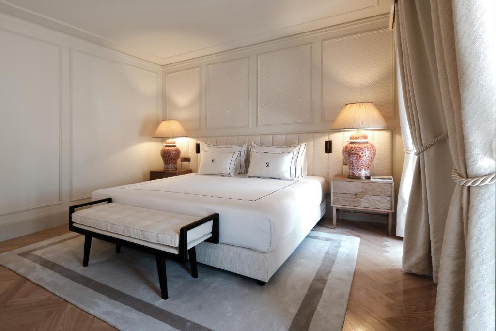 Quarto do GA Palace Hotel com cama de casal no centro do quarto em cada lado da cama uma cômoda com luminária e no pé da cama um banco estofado. Representa hotéis 5 estrelas em Portugal.