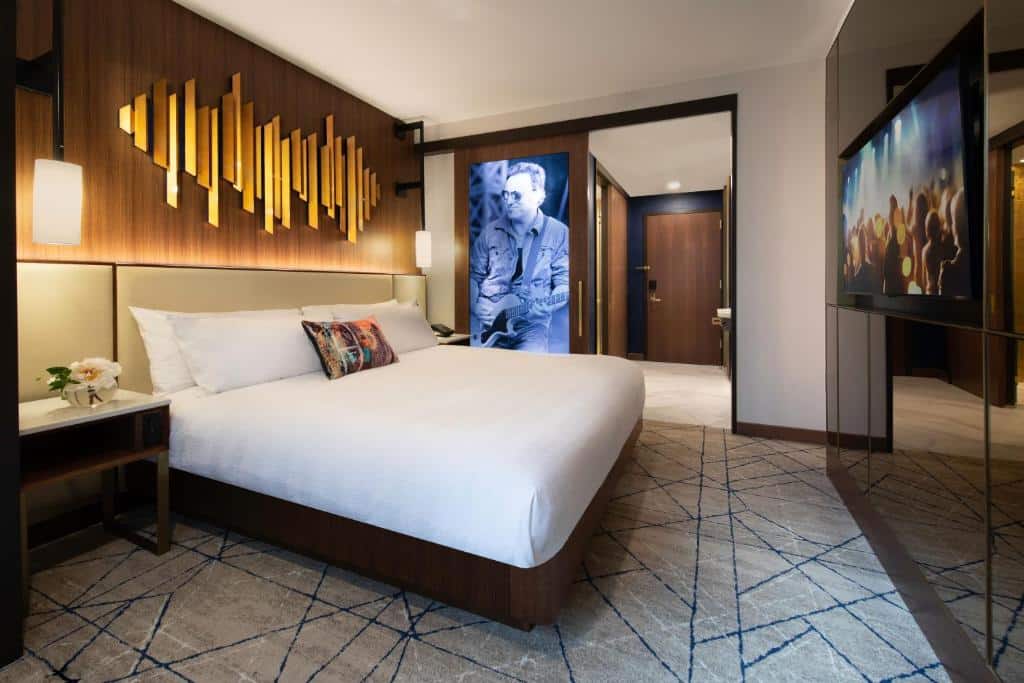 quarto do Hard Rock Hotel New York  hotel perto da times square com uma cama de casal à esquerda, um quadro de um cantor no lado direito da imagem e uma televisão de tela plana em frente a cama, pendurada na parede.