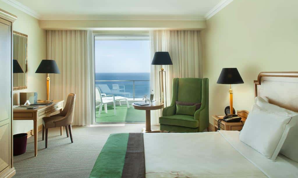Quarto do Hotel Cascais Miragem Health & Spa com cama de casal do lado direito da imagem, do lado esquerdo da cama uma cômoda com telefone e luminária, ao lado da cômoda um sofá com um mesa redonda ao lado. Representa hotéis 5 estrelas em Portugal.