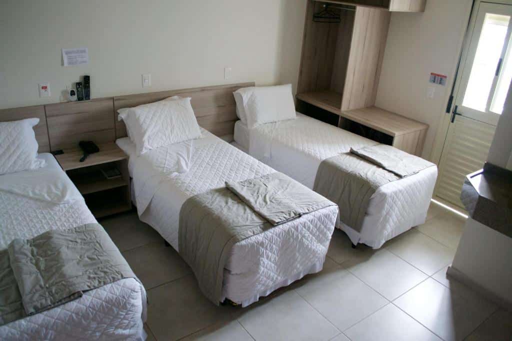 quarto do Hotel Dois H em Joinville com três camas de solteiro dispostas lado a lado em um quarto pequeno. À direito do quarto é possível ver uma porta com acesso ao corredor