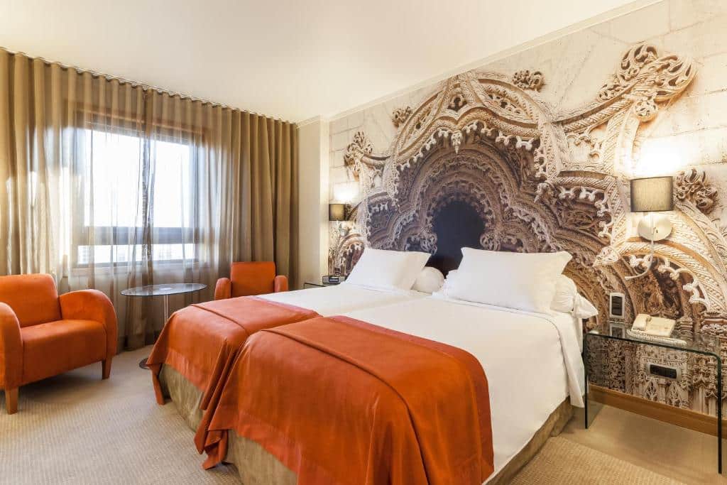 Quarto do Hotel Marques De Pombal com duas camas de solteiro, do lado esquerdo do quarto há uma janela com cortinas, embaixo dela há duas poltronas e uma mesinha redonda, para representar hotéis no centro de Lisboa