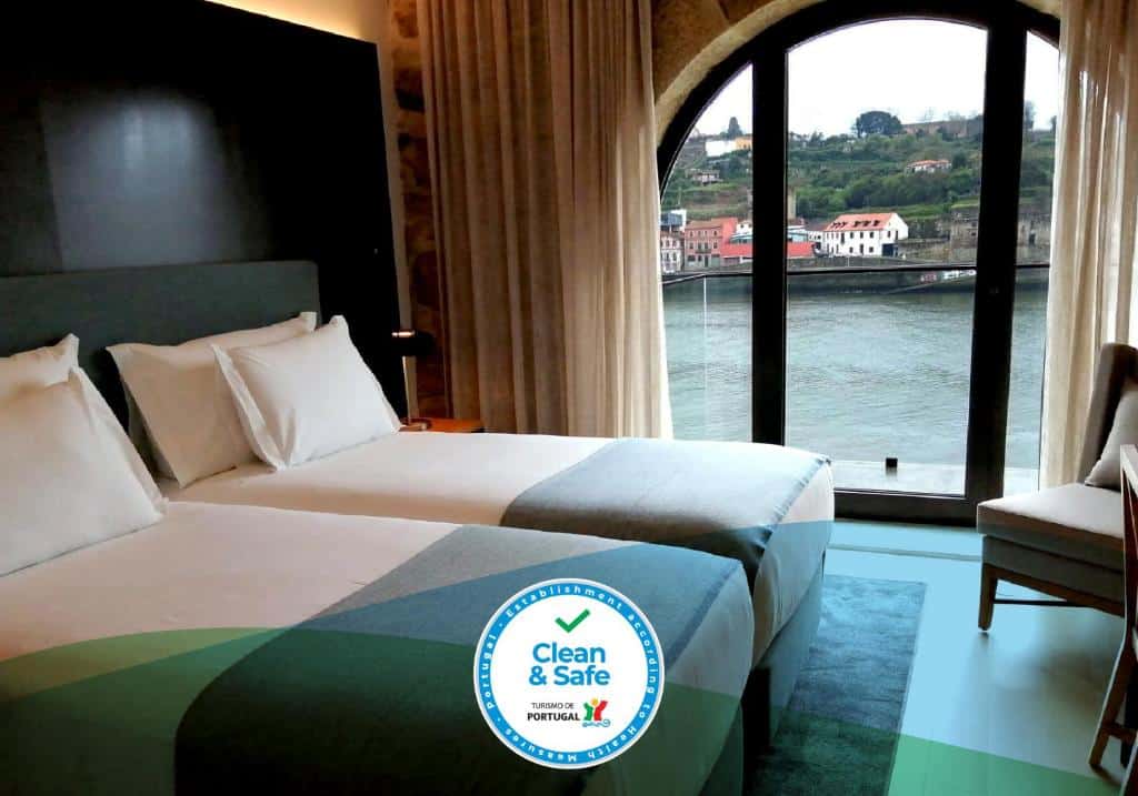 Quarto do NEYA Porto Hotel com dias camas de solteiro do lado esquerdo da imagem, do lado direito uma poltrona e ao fundo janelas panorâmicas com vista para o Douro. Representa hotéis com vista do Douro.