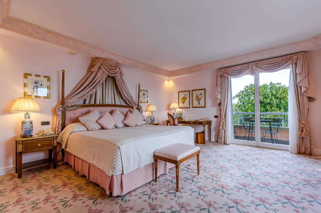 Quarto do Olissippo Lapa Palace – The Leading Hotels of the World com cama de casal do lado esquerdo da imagem com uma cômoda em cada lado da cama com luminária e do lado esquerdo da cama uma mesa de trabalho com cadeira. Representa hotéis 5 estrelas em Portugal.