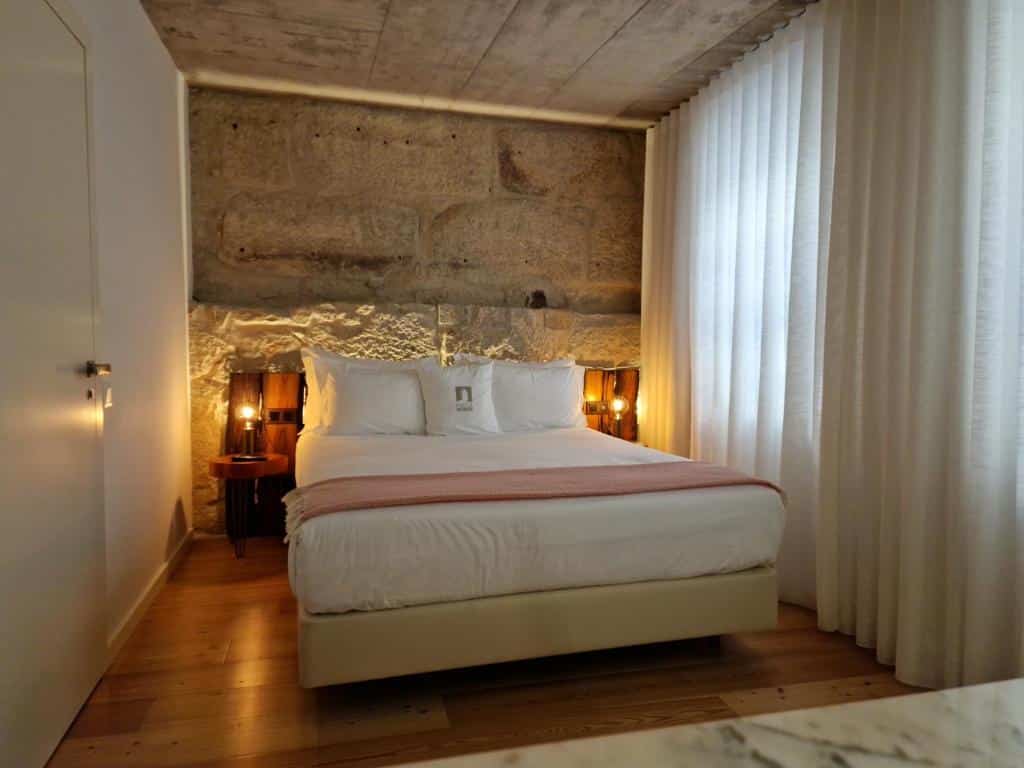 Quarto do Porta Nobre – Exclusive Living Hotel com cama de casal no centro da imagem com uma cômoda em cada lado da cama com luminária. Representa hotéis no centro do Porto.