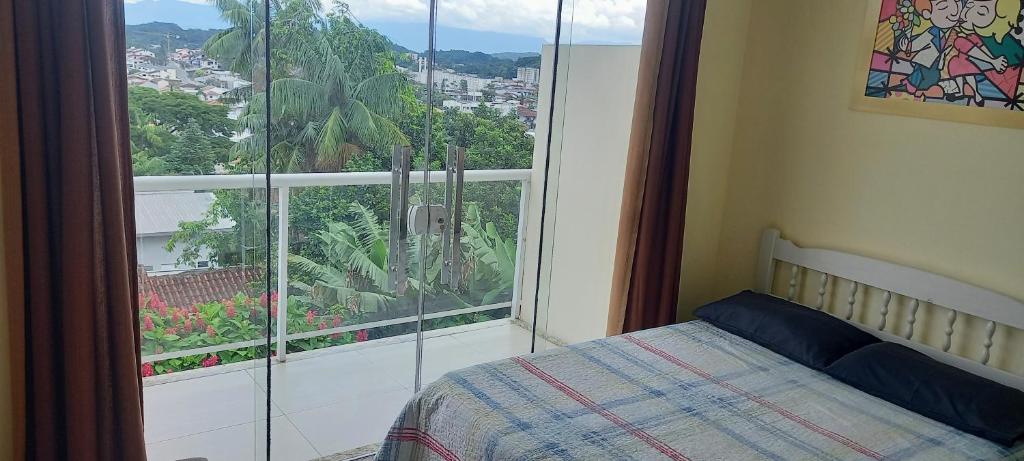 suíte da Pousada Floresta em Joinville com uma cama de casal à direita da imagem, e uma sacada com porta de vidro ao lado esquerdo da cama, com vista para a cidade.
