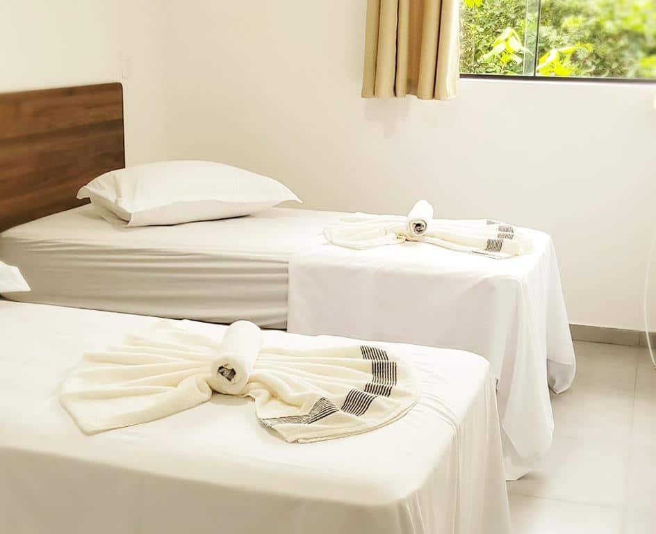 quarto da Pousada São José em Joinville com duas camas de solteiro, equipadas com lençóis e toalhas brancas.