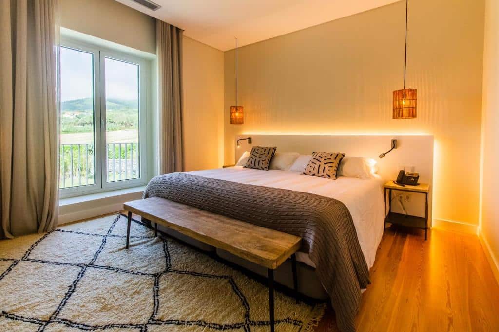 Quarto do SENSI Azores Nature and SPA com cama de casal do lado direito da imagem, com uma cômoda em cada lado da cama e no pé da cama um banco. Representa hotéis 5 estrelas em Portugal.
