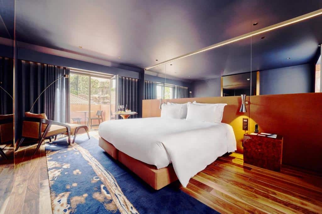 Quarto do The Lodge Porto Hotel com cama de casal no centro do quarto, do lado esquerdo uma poltrona. Representa hotéis 5 estrelas em Portugal.
