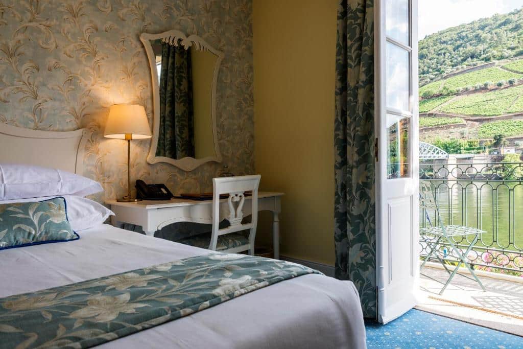 Quarto do The Vintage House – Douro com cama de casal do lado esquerdo da imagem, do lado esquerdo da cama uma mesa de trabalho com cadeira. Representa hotéis 5 estrelas em Portugal.